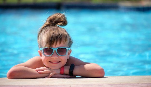 Ragazza felice del bambino che si rilassa sul lato della piscina nella soleggiata giornata estiva