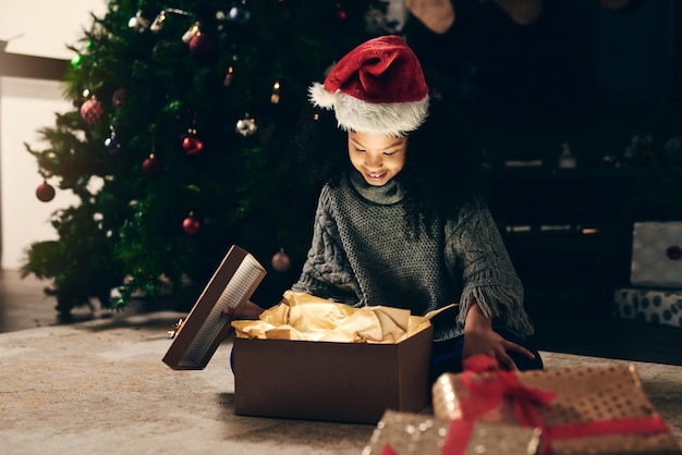 Regalo di Natale e scatola di apertura della ragazza di notte a casa in vacanza Spirito natalizio felice ed eccitato bambino o ragazzo con un sorriso che guarda regali o regali luminosi e si gode le vacanze di dicembre in casa