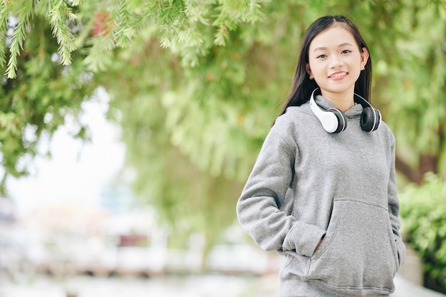 Foto ritratto di un'adolescente asiatica allegra in felpa con cappuccio che sorride e quando balla all'aperto