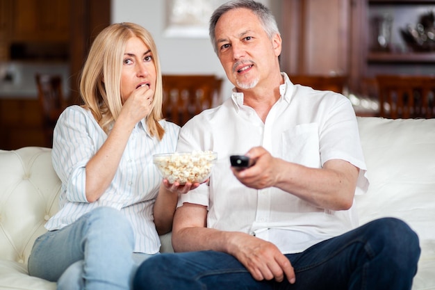 Ritratto di una coppia matura felice nella loro casa guardando la tv insieme