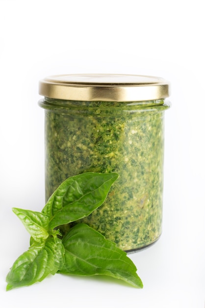 Foto salsa al pesto in un barattolo di vetro isolato con foglie di basilico fresco su sfondo bianco. pesto di salsa italiana tradizionale casalinga e foglie di basilico.