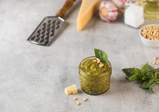 Foto salsa di pesto in un barattolo con noci di pino una fetta di parmigiano e foglie di basilico verde copiare spazio