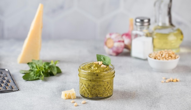 Foto salsa di pesto in un barattolo con noci di pino una fetta di parmigiano e foglie di basilico verde