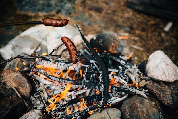 Salsicce alla griglia sopra il fuoco nella foresta estiva