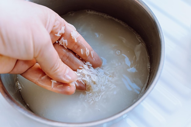 sciacquare il riso prima della cottura. la mano del cuoco lava i chicchi di riso in un mestolo di metallo sotto l'acqua corrente.