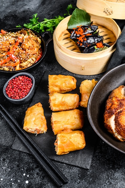 Set di piatti di cucina cinese, sfondo nero di cibo. Tagliatelle cinesi, gnocchi, anatra alla pechinese, dim sum, involtini primavera. Famoso. Vista dall'alto