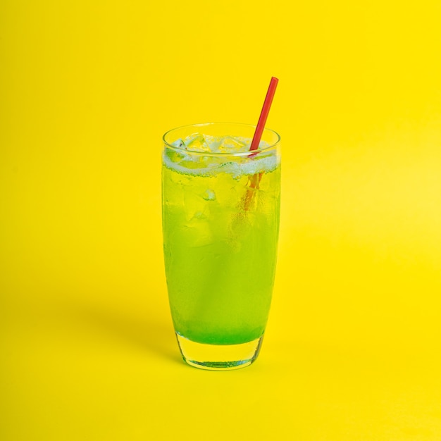 Succo di frullato di cocktail fresco verde in vetro con ghiaccio su sfondo giallo bevanda vitaminica detox