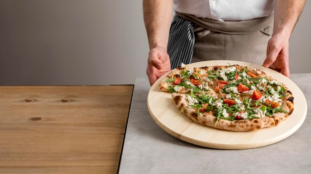 Tagliere della holding dell'uomo di alto angolo con pizza fresca