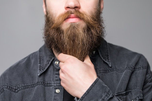 Foto toccandosi la barba perfetta. primo piano di giovane uomo barbuto che tocca la sua barba mentre stando contro il fondo grigio