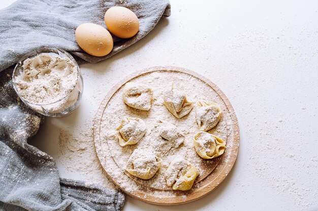 Tortellini o gnocchi italiani sul tagliere di una tavola di legno rotonda cosparsa di farina. processo di cottura