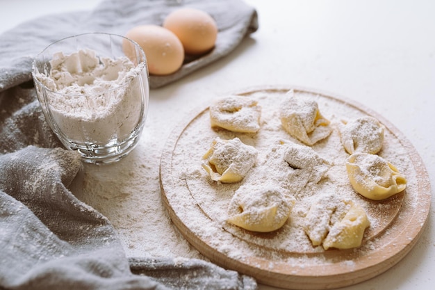 tortellini o gnocchi su un tagliere tondo di legno, spolverati di farina, con gli ingredienti in b