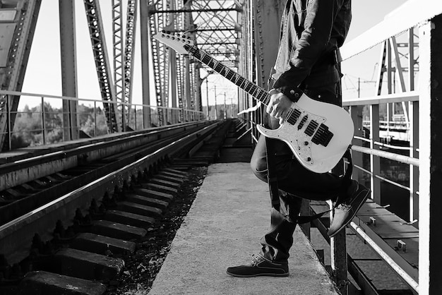 Un uomo con una chitarra elettrica nel paesaggio industriale all'aperto monocromatico