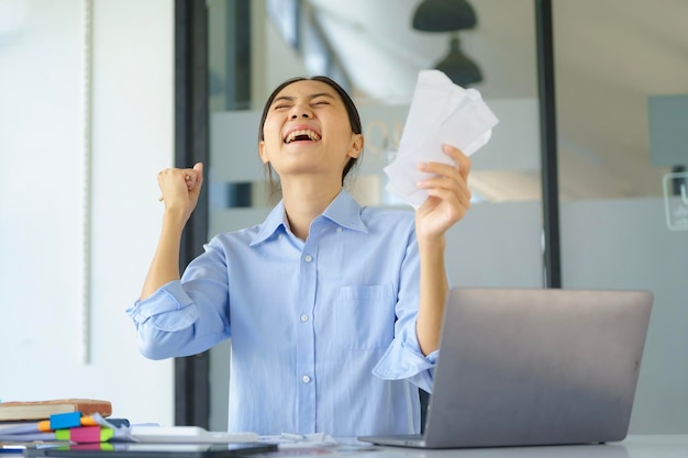 Foto una donna d'affari asiatica che applaude mentre lavora su un portatile in un ufficio