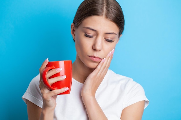 Una giovane donna sente mal di denti e tiene il posto del dolore con le mani