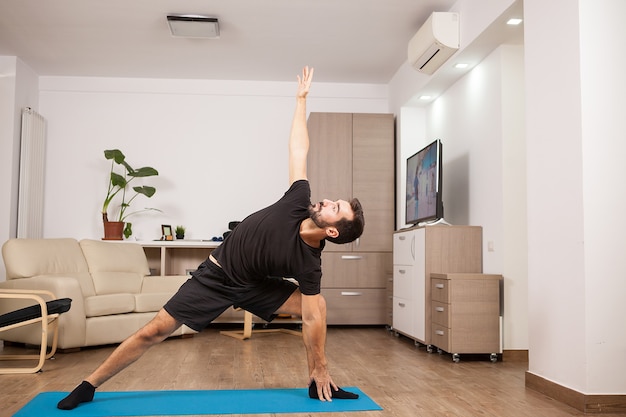 Uomo attraente che prova le pose di yoga laterali estese sul pavimento della sua casa. Allenamento di atletica.