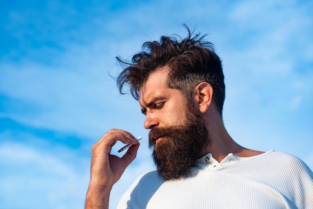 Foto uomo che fuma sigaretta sullo sfondo del cielo. ragazzo brutale.