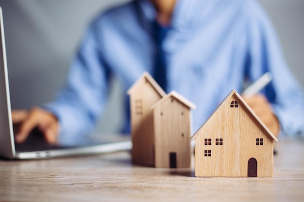 Uomo d'affari che sceglie il mini modello di casa in legno dal modello sul tavolo di legno Pianificazione di acquistare il concetto di proprietà di Scegli il meglio