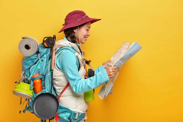 Foto grátis a turista asiática estuda o mapa, encontra um novo destino para explorar, viaja sozinha, usa boné e roupa ativa, carrega uma mochila grande