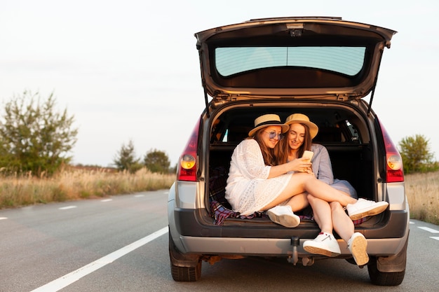 Amigas olhando para o smartphone no porta-malas do carro