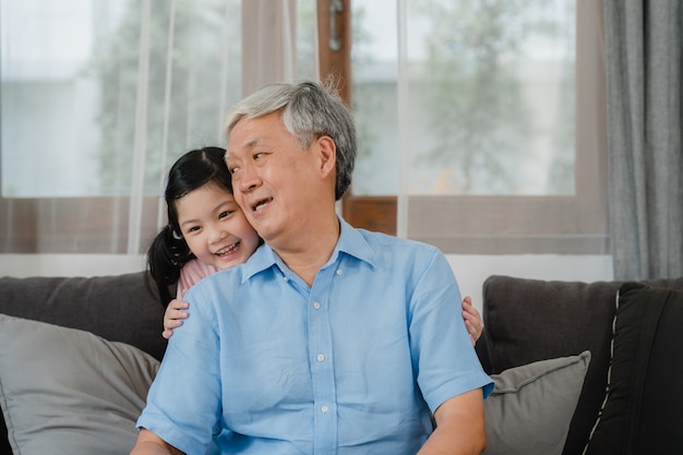 Foto grátis avô asiático que fala com neta em casa. o chinês sênior, vovô feliz relaxa com a menina nova da neta que usa o tempo da família relaxa com criança da moça que encontra-se no sofá na sala de visitas.