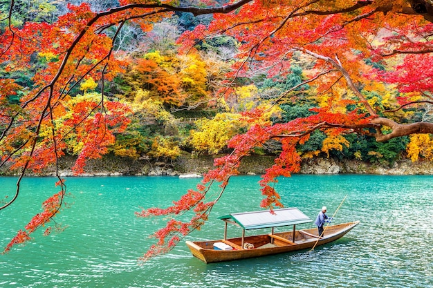 Foto grátis barqueiro rebatendo o barco no rio. arashiyama na temporada de outono ao longo do rio em kyoto, japão