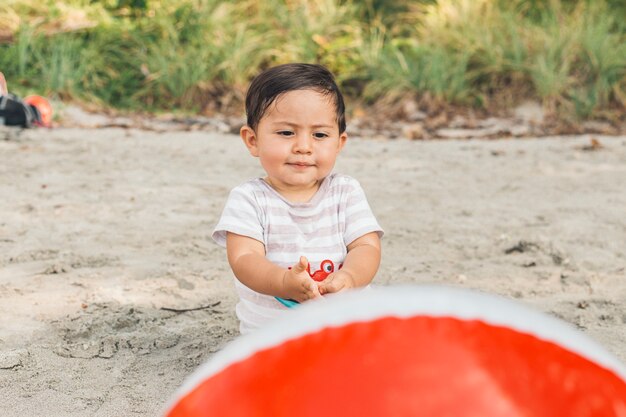 Bebê fofo brincando com bola na praia