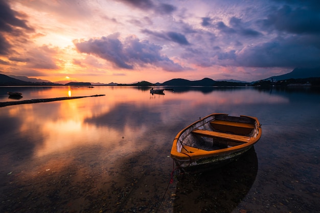 Bela foto de um pequeno lago com um barco a remo de madeira em foco e nuvens de tirar o fôlego no céu