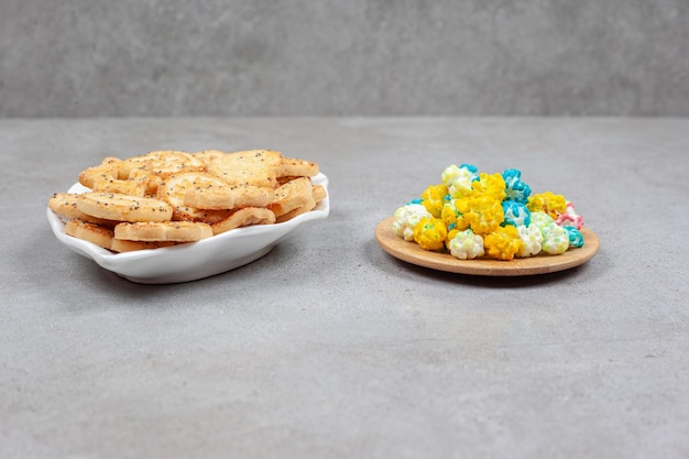 Foto grátis biscoitos em um prato ornamentado ao lado de uma pequena bandeja de madeira com doces de pipoca na superfície de mármore.