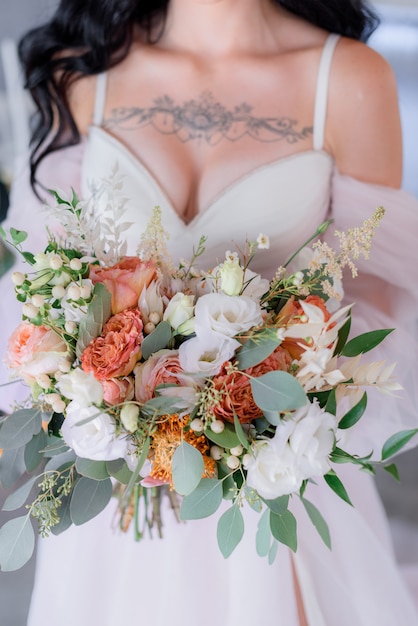 Buquê de casamento de eustoma e eucalipto, vestido de noiva com decote aberto e tatuagem nos seios