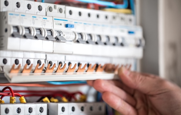 Cara, um eletricista trabalhando em uma central telefônica com fusíveis. Instalação e conexão de equipamentos elétricos. Fechar-se.