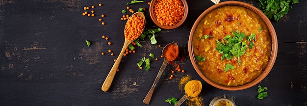 Caril picante indiano Dhal na tigela, especiarias, ervas, mesa de madeira preta rústica.