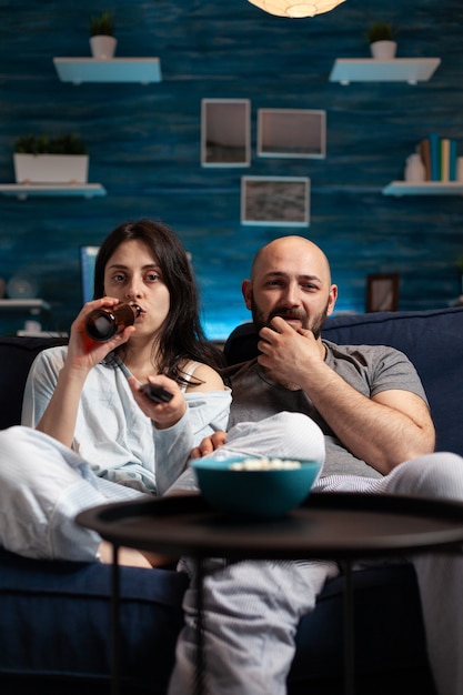 Foto grátis casal animado e relaxado assistindo tv no sofá e relaxando tarde da noite