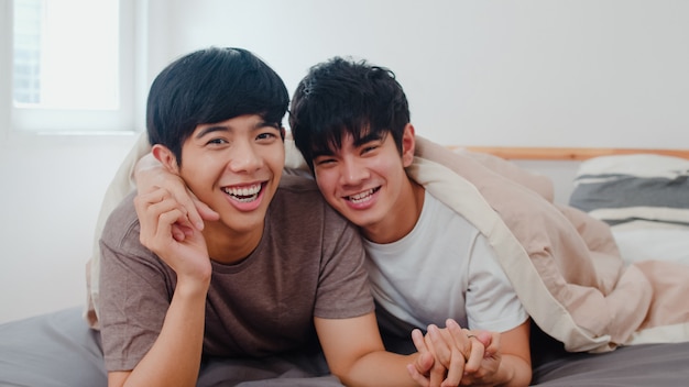 Foto grátis casal gay asiático novo do retrato que sente feliz em casa. os homens da ásia lgbtq + relaxam o sorriso, olhando para a câmera enquanto descansam juntos e passam um tempo romântico depois de acordar no quarto na casa moderna pela manhã.