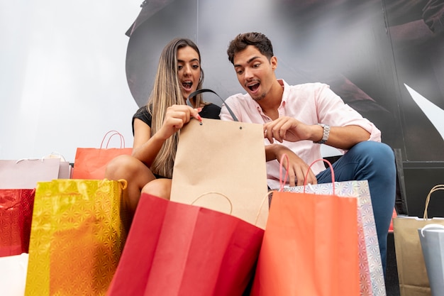 Foto grátis casal jovem espantado, olhando para dentro de sacos de compras