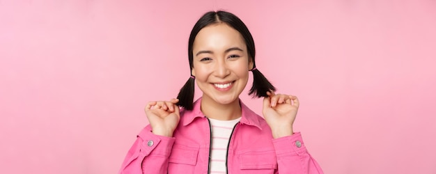 Foto grátis conceito de cuidados com a pele e cosmetologia linda garota asiática sorrindo e rindo mostrando pele facial limpa e saudável posando contra fundo rosa