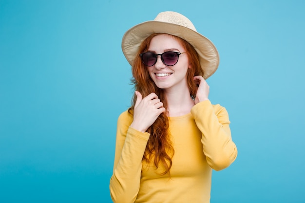 Foto grátis conceito de viagem - close up retrato jovem e bonita menina redhair atraente com chapéu de moda e sorvete sorrindo. fundo pastel azul. copie o espaço.