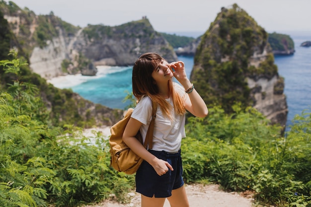 Foto grátis conceito de viagem e aventura. mulher feliz com mochila viajando pela indonésia, na ilha de nusa penida.