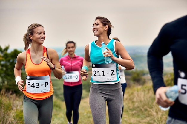 Corredores femininos felizes falando enquanto correm maratona na natureza