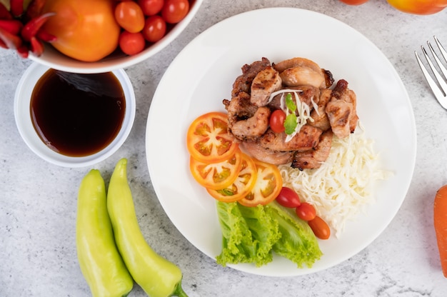 Foto grátis costeleta de porco grelhada com tomates e salada, dispostos em um prato branco.