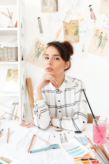 Designer de moda jovem bonita sentada em sua mesa de trabalho