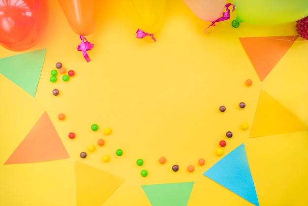 Foto grátis doces coloridos com bunting e balões em fundo amarelo