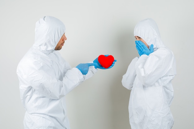 Foto grátis dois médicos em traje de proteção, luvas dando coração vermelho um ao outro