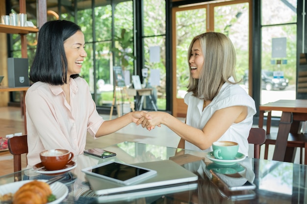 Foto grátis duas empresárias apertando as mãos no café local. duas mulheres discutindo projetos de negócios em um café enquanto tomava um café. conceito de inicialização, ideias e tempestade cerebral. usando laptop no café.