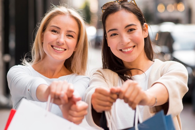 Duas mulheres exibindo sacolas de compras desfocadas após uma maratona de compras