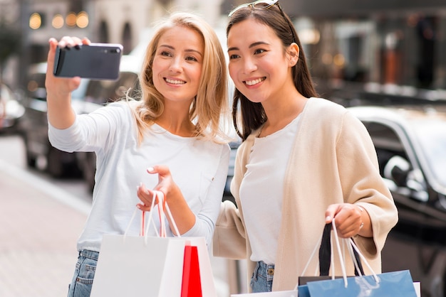 Duas mulheres tirando uma selfie segurando muitas sacolas de compras