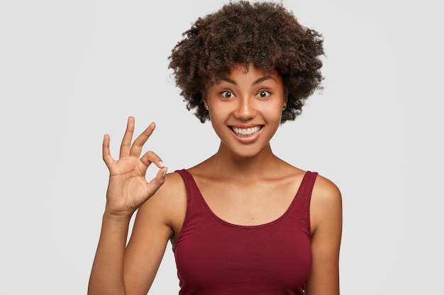 É um acordo. Que bom que mulher bonita com penteado afro, pele morena, sorriso agradável, mostra um gesto bem ou perfeito