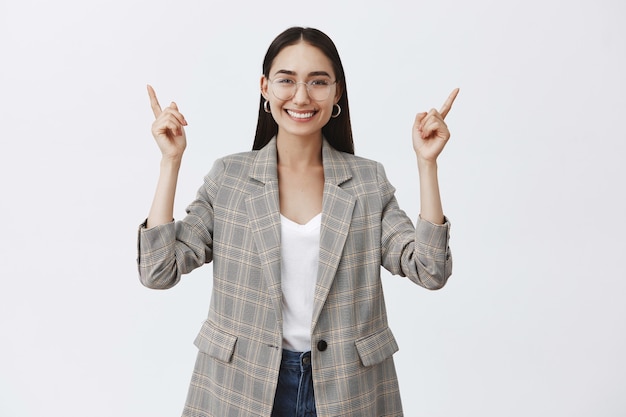 Foto grátis elegante otimista empresária adulta de óculos e jaqueta da moda, levantando as mãos e apontando para cima enquanto sorri amplamente