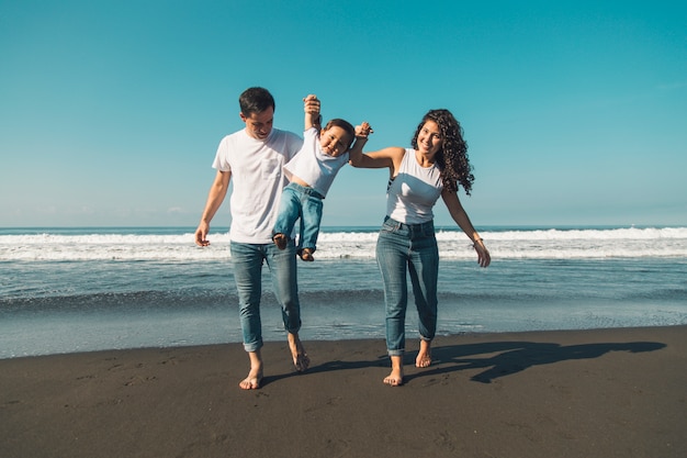 Família jovem feliz se divertindo com o bebê na praia ensolarada