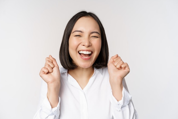 Foto grátis feche o retrato do rosto de uma mulher asiática dançando sorrindo triunfando e comemorando com emoção feliz em pé sobre fundo branco copie o espaço