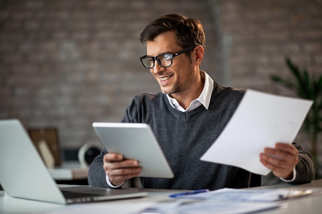 Foto grátis feliz empresário usando touchpad e laptop enquanto trabalhava em relatórios de negócios no escritório